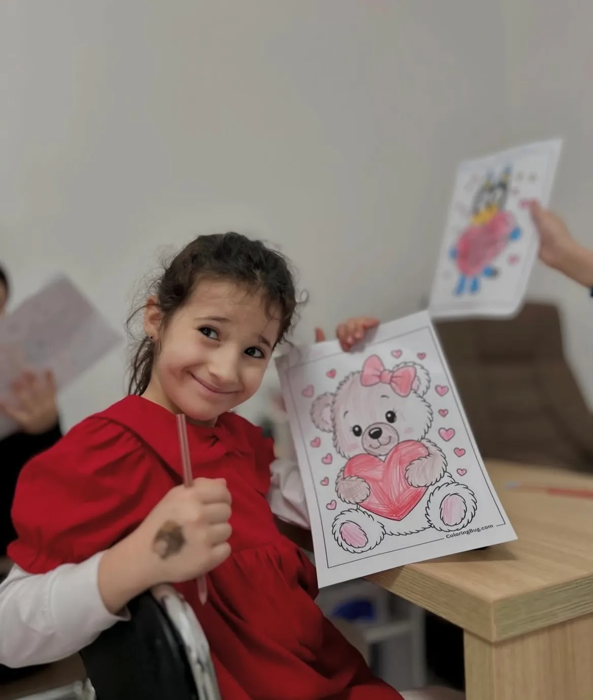 O fetiță arată bucuroasă desenul ei colorat, la o întâlnire de grup